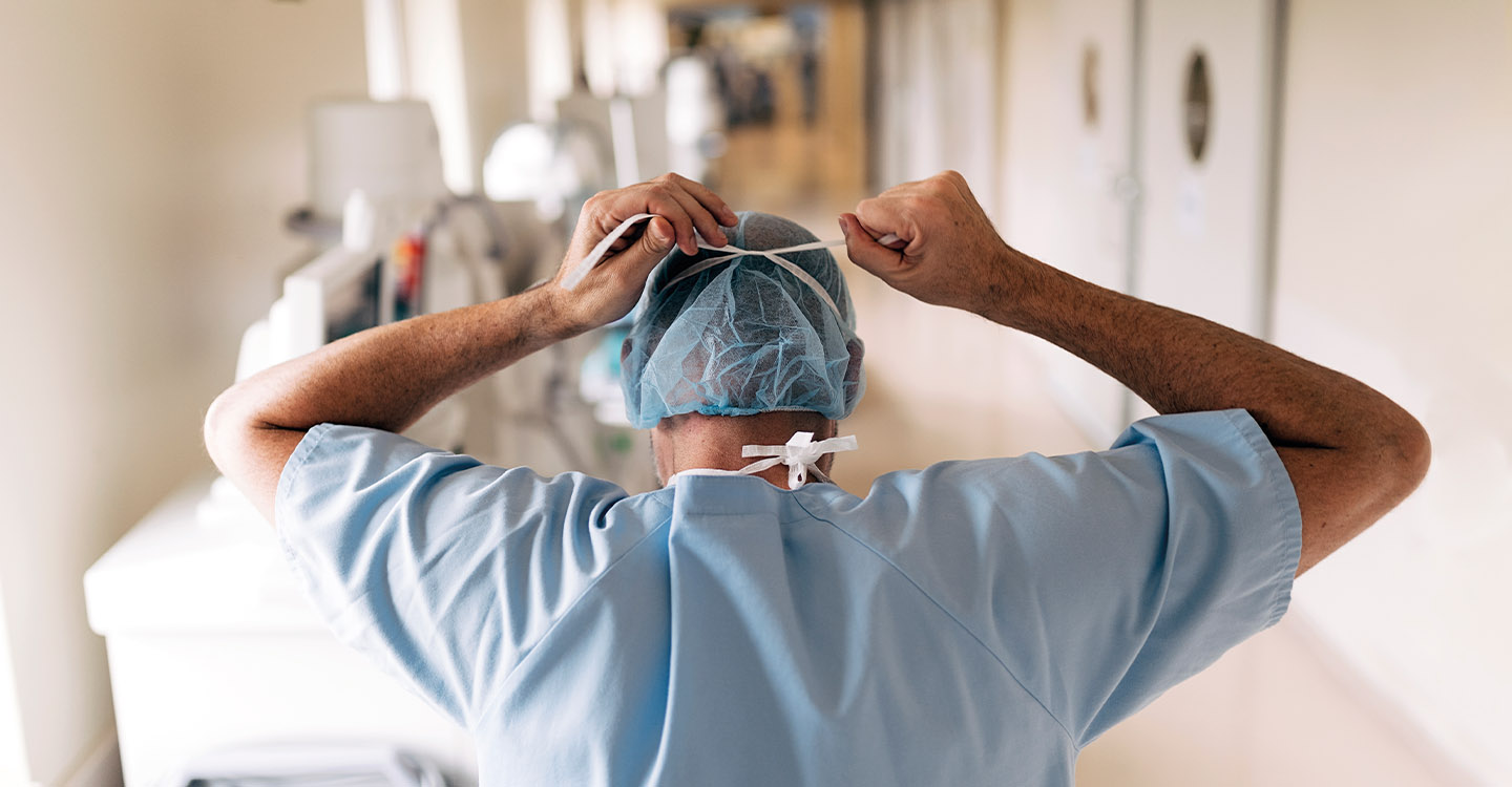 Photo d'un docteur de dos en blouse réajustant son masque dans un couloir d'hôpital